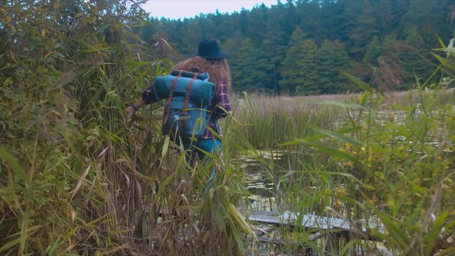 Active healthy Caucasian woman with a backpack taking pictures with an vintage film camera on a forest lake. 4K UHD RAW edited footage