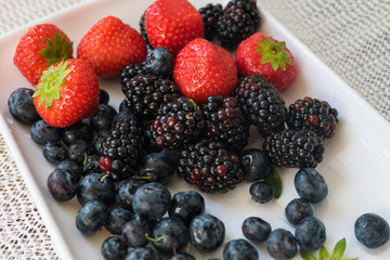 mix berry strawberry blackberry blueberry with red black blue. food flesh berry from nature with green leaf on white plate ready to eat.