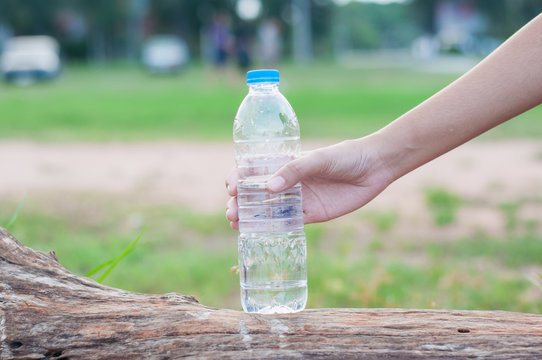 Girl's hand taking water bottle in garden,soft focus.