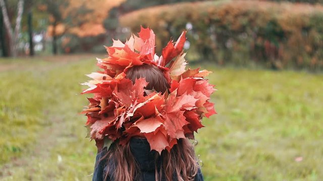 Girl goes back and then turns around and looks at the camera. cute little girl in a wreath crown of autumn maple leaves.