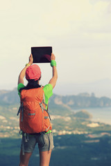 hiker taking photo with digital tablet at seaside mountain top