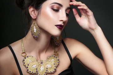 Beauty portrait of a brunette in jewelry on a black background.