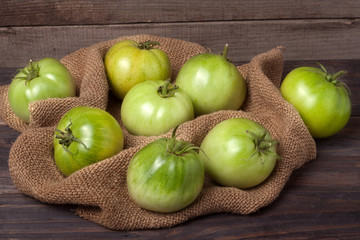 Naklejka na ściany i meble some green unripe tomato on the wooden background with burlap