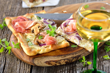 Elsässer Flammkuchen mit Zwiebeln, Pilzen und Serrano-Schinken rustikal auf Holzbrett serviert, dazu Elsässer Wein - Tarte Flambée from Alsace with serrano ham, served with local wine