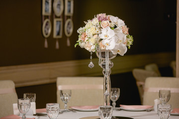 Pretty white bouquet stands in a high vase in the middle of dinn