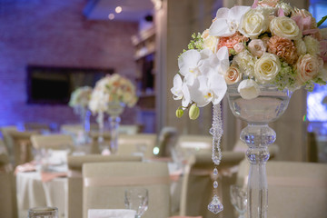 Pastel flowers stand in a high glass vase decorated with crystal