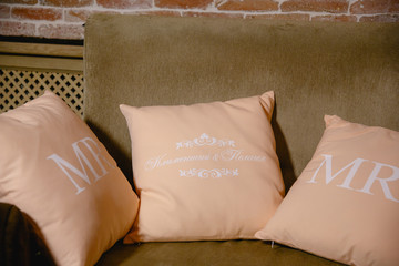 Pink pillows with initial letters lie on a brown sofa