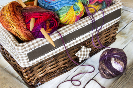 Colorful skeins of wool in knitting basket and needles on wooden background