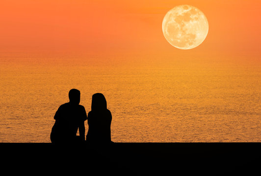 silhoutte rear view romantic couple sit relaxing on the beach in sunset  with full moon 