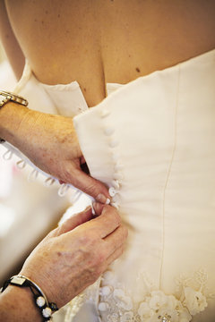 A woman buttoning the back of a bride's white wedding dress. 