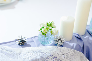 Candles and little bouquet stand on a violet cloth behind a whit