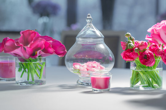 Pink rose petals lie in a glass bowl between flower bouquets
