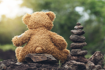 Cute Teddy bear sitting on the rock with Stones stacked layers a