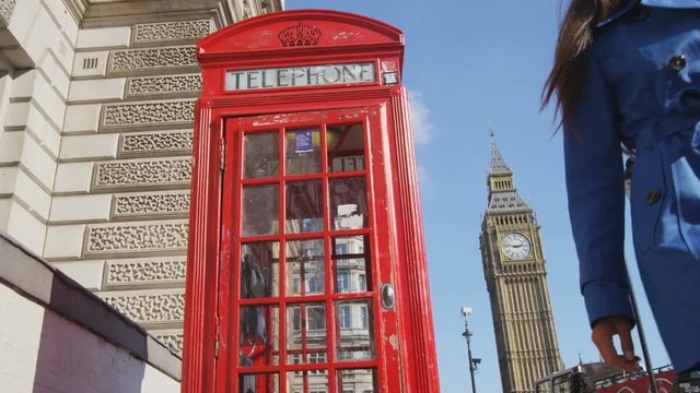 Young female urban professional using mobile smart phone by red telephone booth in London, England, Great Britain. Happy young woman is walking by Big Ben enjoying leisure time in United Kingdom.