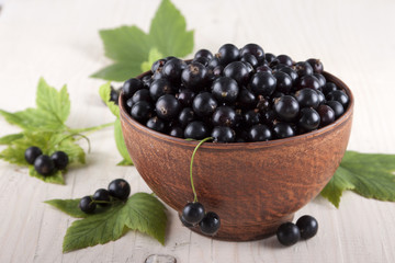 Black currants in a ceramic bowl on the white wooden table