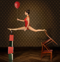 A girl is doing the splits. There is red balloon in her hand.