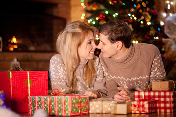 Couple in love on the background of New Year and Christmas lights near the burning fireplace consider Christmas gifts