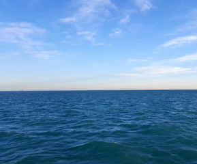 Fototapeta na wymiar Blue Ocean Water Meets Blue Sky With Clouds