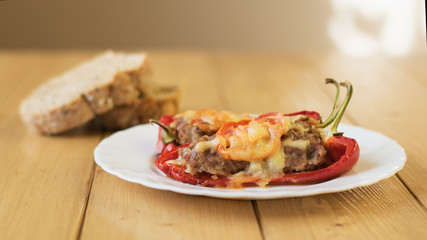 Baked pepper with meat, cheese and tomato on the plate on a wooden table.