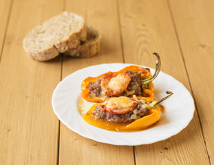Baked pepper with meat, cheese and tomato on the plate on a wooden table.