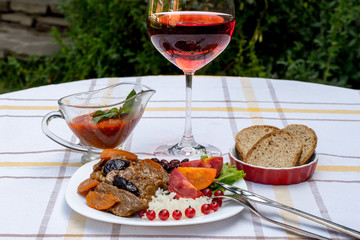 Beef stew with carrot and dried plum, topping with rice, beans and tomatoes. Served on a white plate with crusty bread, home made sauce and glass of red wine.