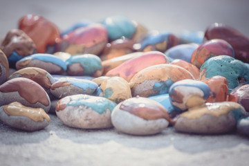 Many small pebbles covered with multicolored paint lie on surface