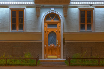 Two windows and door in a row on night illuminated facade of urban apartment building front view,...