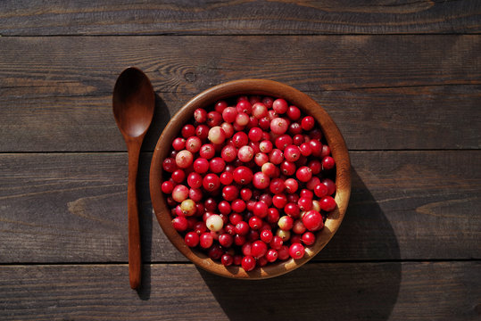 Fresh red forest cranberry in a round bowl with a wooden spoon on a table surface. Autumn harvest of wild berries