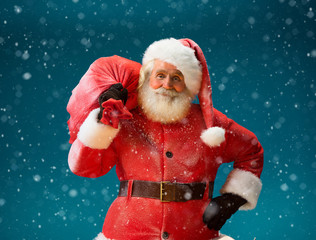 Smiling Santa Claus carrying big bag full of gifts to children on blue background. Merry Christmas & New Year's Eve concept. © Romario Ien