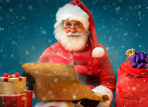 Kind Santa Claus with vintage list and gifts on blue background. Merry Christmas & New Year's Eve concept.
