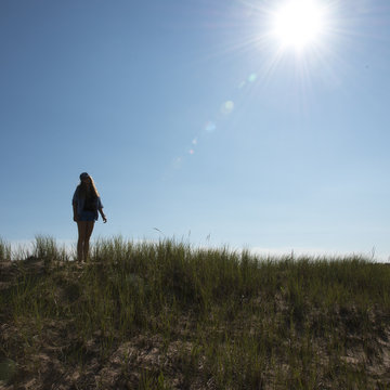 Girl standing on grassy sand dune under bright sunshine at Caven