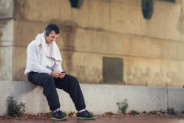 Young athelete is having a brake from exercising and using his smarphone.