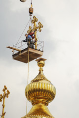 Fototapeta na wymiar builders lifted on a crane large gold cross to be installed on the dome of the Orthodox church.