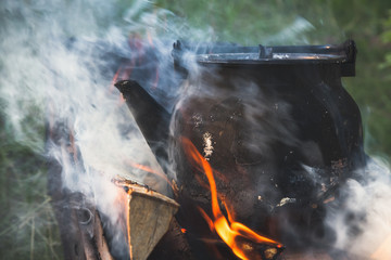Teapot with boiling water stands on a bonfire