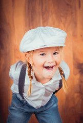 Children's emotions. Artistic little girl in jeans with suspenders, white shirt and a cap on the...