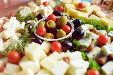 Olives, white and yellow cheese and tomato on wooden plate