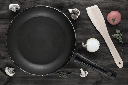 empty pan with mushrooms , tomato, garlic, onion, parsley leaves and wooden spatula on wooden table