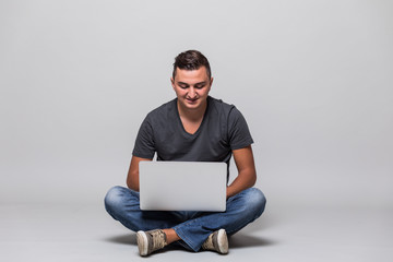 Happy casual man sitting on the floor with laptop over gray background