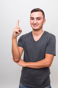 Portrait of young handsome smiling carismatic man having an idea and pointing finger up isolated on a grey background