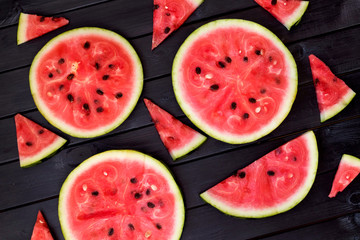 Background of fresh ripe watermelon slices on black wooden table. Top view.