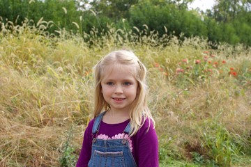 adorable young girl wearing overalls standing on field on farm