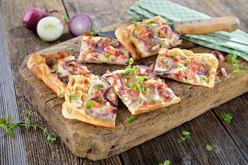 Elsässer Flammkuchen mit Zwiebeln und Speck rustikal auf altem Schneidbrett serviert - Traditional Alsatian tarte flambée  with onions, bacon and sour cream served on a shabby cutting board