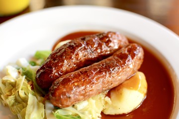 Sausage and mashed potato with seasonal greens served with red wine gravy on a white plate