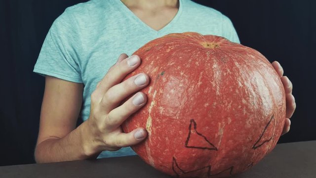 Guy in white t-shirt holding pumpking with drawn face, then put it down and make a creepy smile