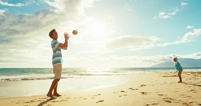 Father and son having fun on the beach at sunset, playing catch with football