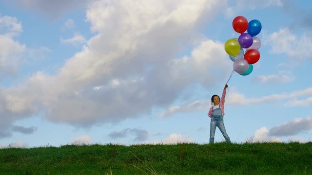 Young child stands on grass holding multiple balloons, in slow motion - with copy space