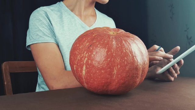 Guy in white shirt use picture on tablet computer as reference and draw on pumpkin jack o lantern 4k