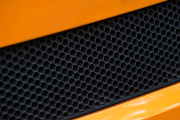 Car grill detail on luxury sport orange and black car.