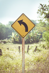 Turn road sign with country side background.