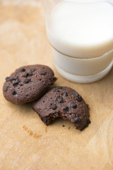 Chocolate chip cookies and glass of milk on wooden plate